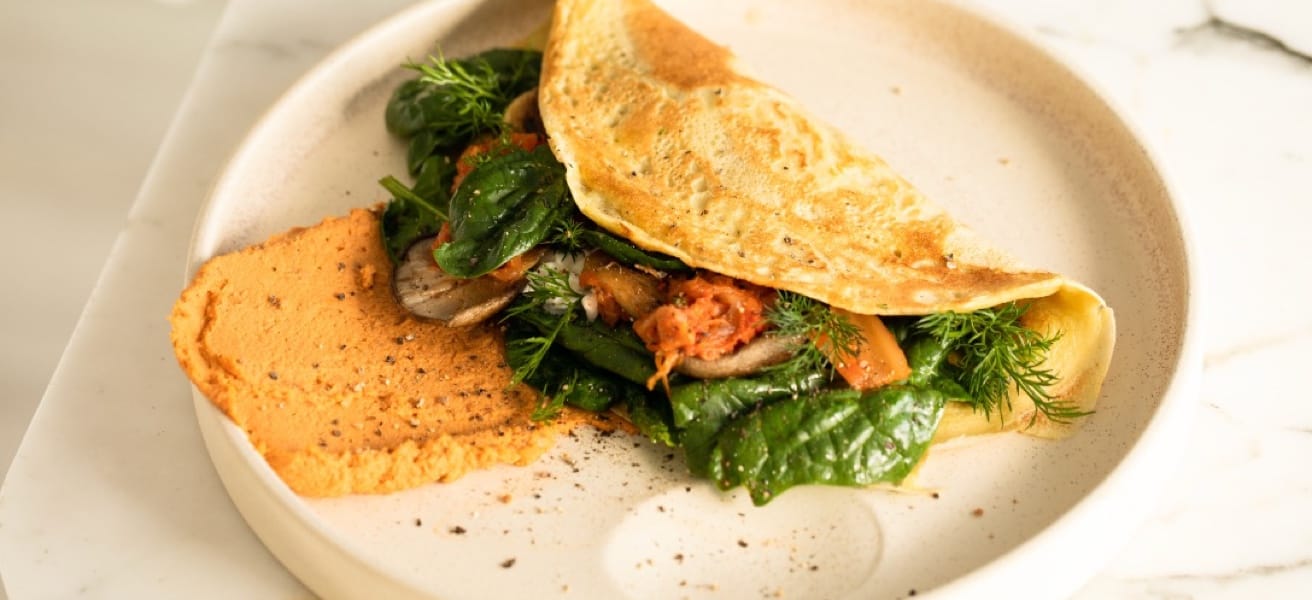 A cooked omlette on a white plate, filled with vegetables and meat